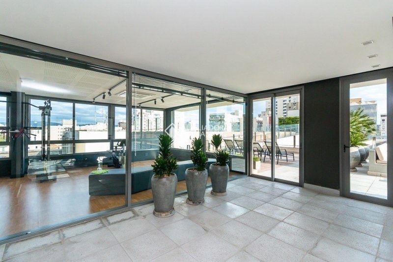 A spacious terrace area is showcased, framed by large glass walls that allow natural light to fill the space. Potted plants are positioned around the area, complementing the modern furnishings inside. The terrace features a view of the surrounding cityscape.
