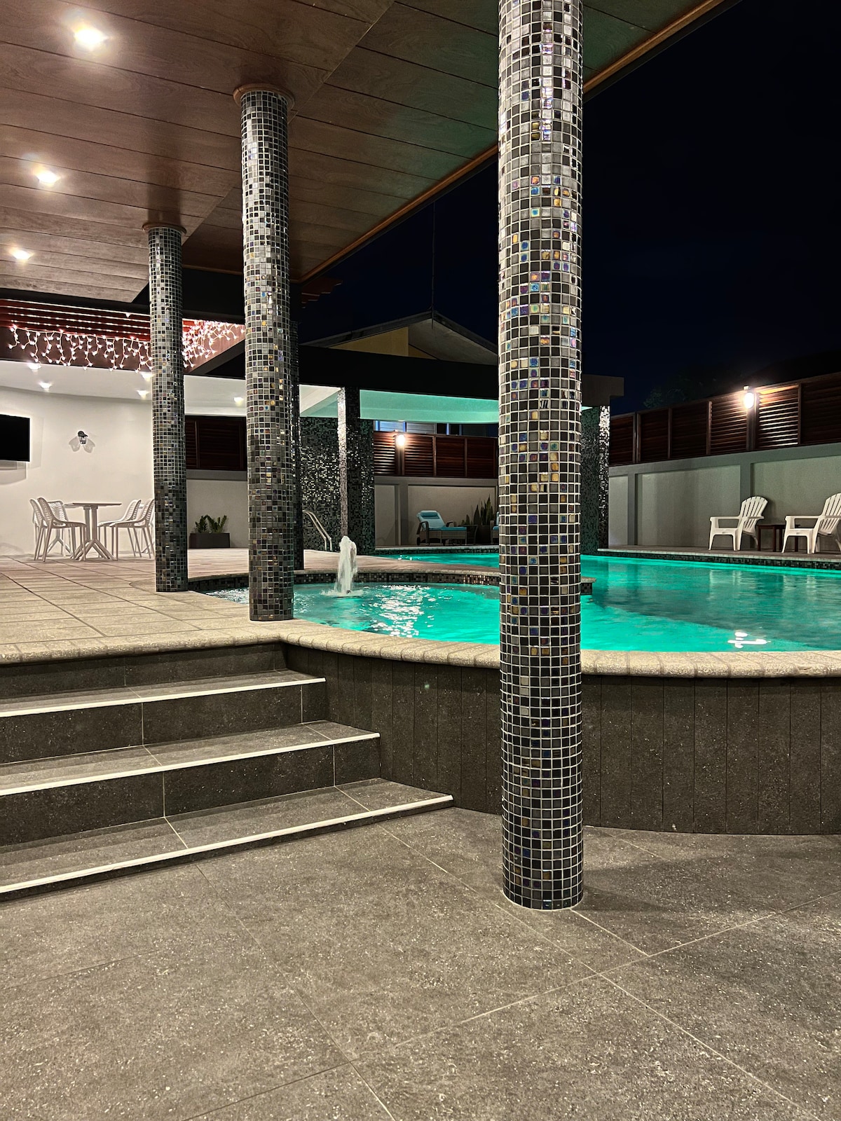 A swimming pool is showcased, surrounded by tiled columns and illuminated by soft lighting. Comfortable seating areas are arranged nearby, creating a relaxing outdoor space. The atmosphere reflects a serene environment, enhanced by the gentle glow of the water.