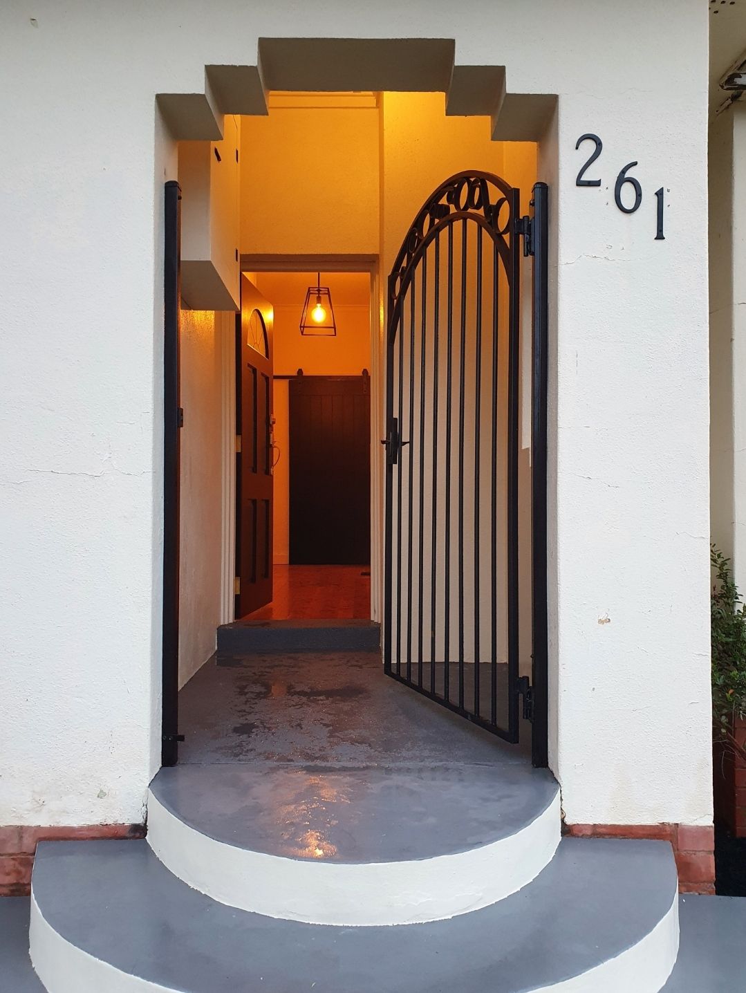 An inviting entrance is depicted, showcasing a curved staircase leading to a secure, wrought-iron gate. Soft illumination highlights the welcoming path, while a decorative lantern hangs above, enhancing the entryway's charm.
