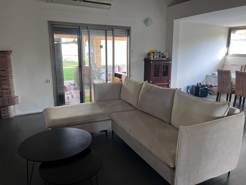 A spacious living room features a light-colored sectional sofa paired with a sleek black coffee table. Large glass doors provide access to a patio, allowing natural light to enhance the room. A dining area is visible in the background, with a neutral color palette throughout.