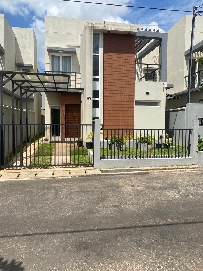 The exterior of the residence features a modern façade with a combination of textured brick and smooth white walls. A well-maintained garden is visible in front, framed by a gated entrance. Ample natural light is captured through large windows, enhancing the inviting atmosphere.