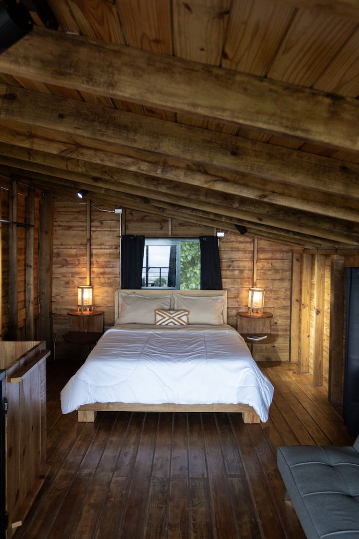 غرفة النوم الرئيسية تحت عوارض خشبية
غرفة نوم رئيسية بسرير مريح وإضاءة دافئة وسقف خشبي، مما يخلق جوًا ريفيًا ورومانسيًا في وسط الجبل.