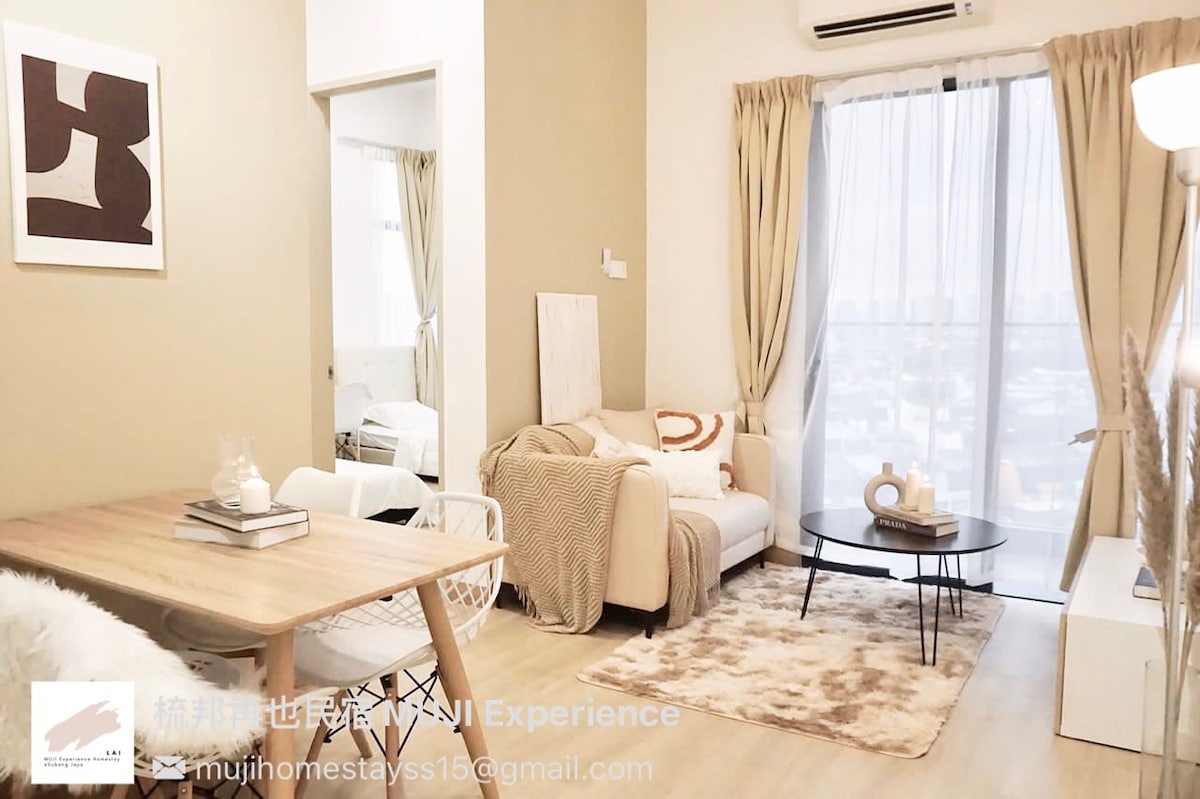 The cozy living area features a light-colored sofa accented with soft cushions and a neutral area rug. A wooden dining table with white chairs is positioned next to large windows, allowing natural light to brighten the space, complemented by soft drapes.