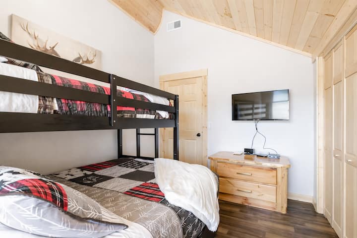 Inviting bunk bedroom with warm wood finishes, vaulted ceiling, natural light create a comfortable cabin feel, and enjoy movie nights with the wall-mounted TV.