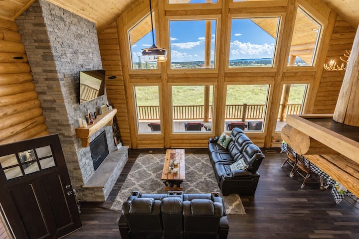 Beautiful great room with floor-to-ceiling windows, leather seating, and a stone fireplace overlooking wide-open views.