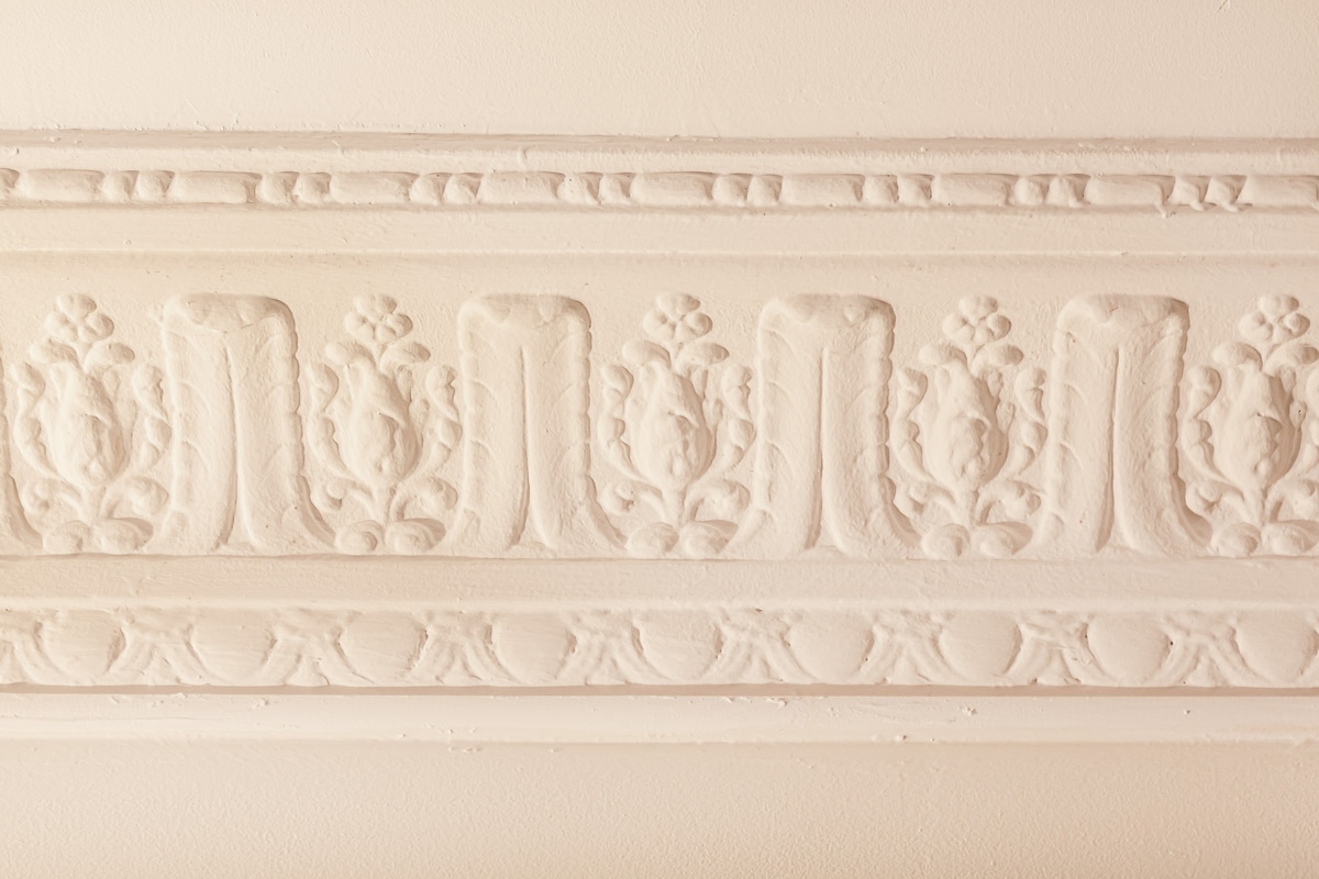 A decorative ceiling molding is presented, featuring intricate floral designs and patterns. The craftsmanship highlights a white plaster texture, enhancing the elegance of the space. The clean lines and detailed relief create a sense of depth and character within the room.