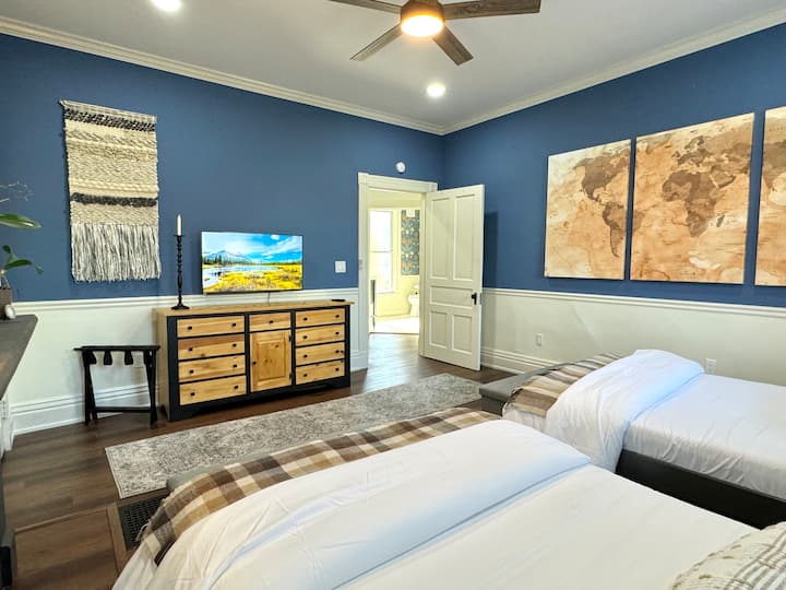 In a bedroom adorned with dual double beds, a faux fireplace imparts the idea of warmth. World map wall art whispers of adventures, creating a haven for shared dreams and tranquil nights.