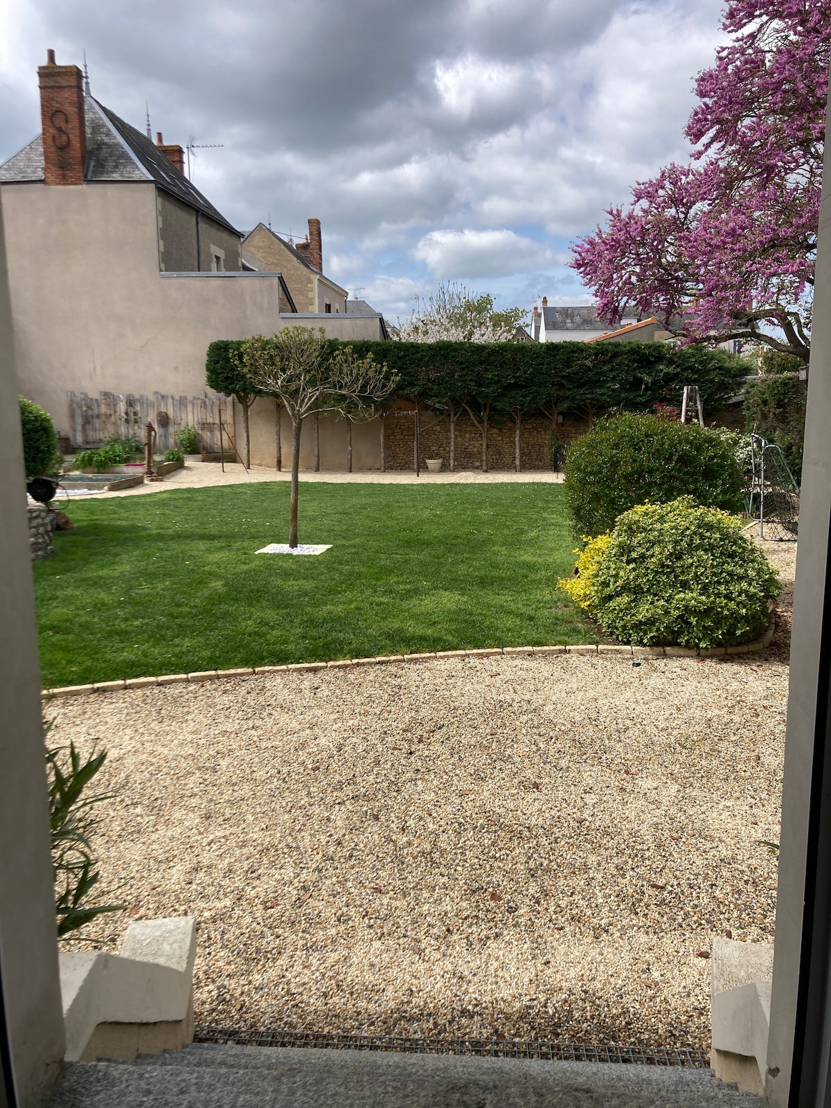 A spacious garden is featured, characterized by lush green grass and well-maintained shrubbery. Flowering trees and a decorative stone pathway add to the landscape. An outdoor seating area is visible, offering a tranquil space for relaxation.