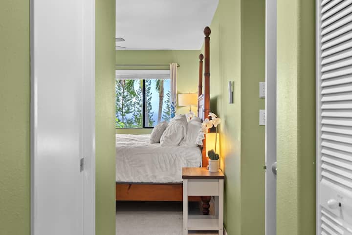 Master bedroom with large picture window facing beautiful ocean views and palm trees. This room has a king bed, new split AC unit and fan, work space, 50-inch smart TV, and in-suite master bathroom.