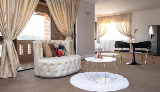 A stylish seating area features a round, cream-colored couch adorned with decorative pillows. A circular coffee table stands on a soft area rug, while large windows allow natural light to fill the room, creating a bright and airy atmosphere.