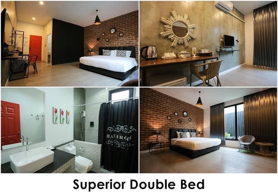 A modern room features a spacious double bed set against a textured wall. A stylish workspace with a chair and desk is visible, complemented by natural light from large windows. The bathroom showcases a sleek double sink and a walk-in shower, accented by brick details.