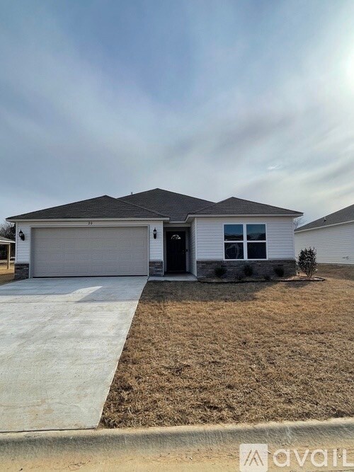 A single-story home with a light-colored exterior and a pitched roof is presented. The driveway leads to a two-car garage, and the front yard features a simple landscape with grass and low shrubbery. Large windows allow natural light to fill the interior.