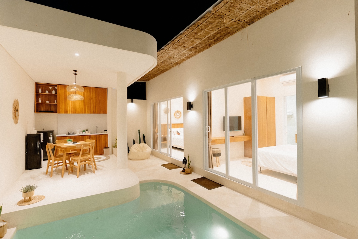 A modern outdoor space features a private pool surrounded by a relaxing atmosphere. An open-plan kitchen and dining area are visible, complemented by a cozy dining table. Floor-to-ceiling glass doors connect the indoor living area and sleeping quarters, creating a seamless flow of light.