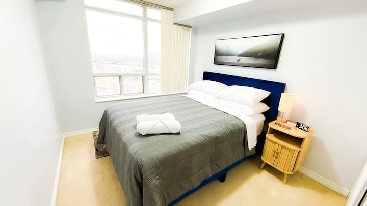 Cama tamaño queen Sealy posturepedic de firmeza media en el segundo dormitorio. Y una mesa auxiliar con una estación de carga de dispositivos incorporada. 