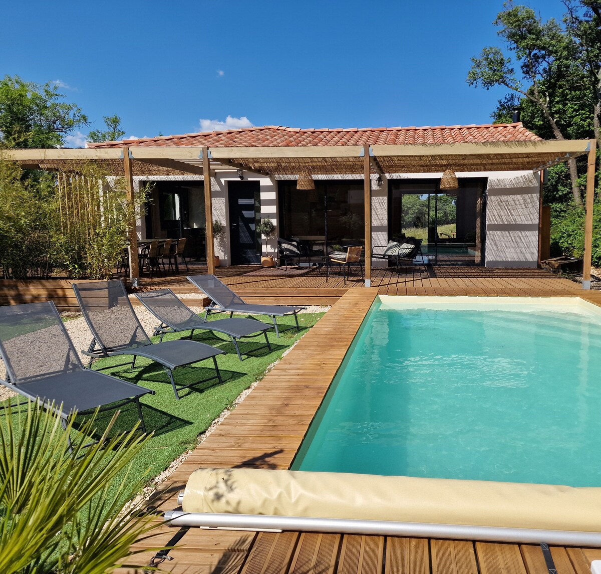 A refreshing private pool is set within a spacious wooden deck, surrounded by lounge chairs for relaxation. Bamboo and greenery enhance the outdoor space, while the elegant house is visible in the background, seamlessly connecting indoor and outdoor living.