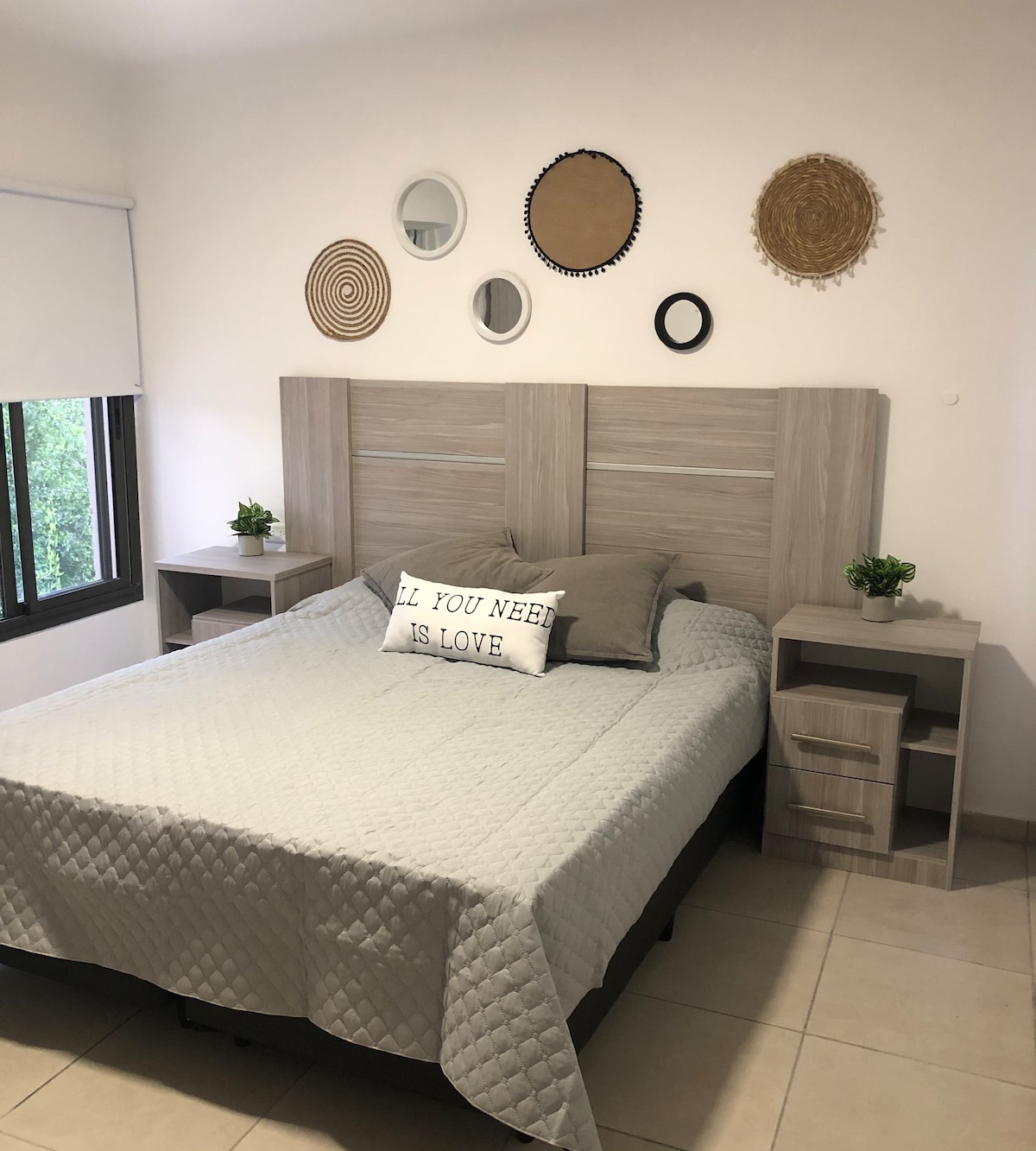 A tranquil bedroom is furnished with a spacious bed layered with a light quilt and accented by decorative pillows. Tasteful wall art and plants are arranged above the headboard, while side tables frame the bed, complementing the calm color palette.