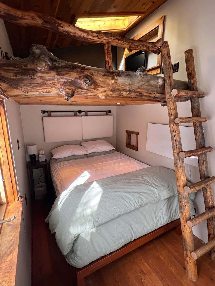 Una acogedora cama tamaño queen está escondida bajo un loft personalizado estilo casa de árbol 