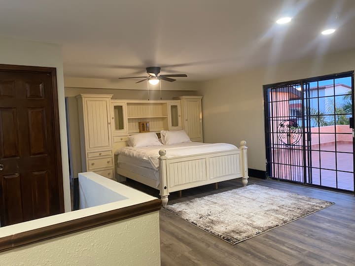 غرفة النوم الرئيسية الواسعة السادسة، منطقة خلع الملابس + سرير بحجم كال كينج + سرير بحجم كوين إضافي، مدفأة مع حمام كامل. يمكنك الوصول إلى التيرازا بإطلالة خلابة على المحيط.  تحتوي الغرفة على درج يقودك إلى المطبخ ويتصل بغرفة نوم أخرى.