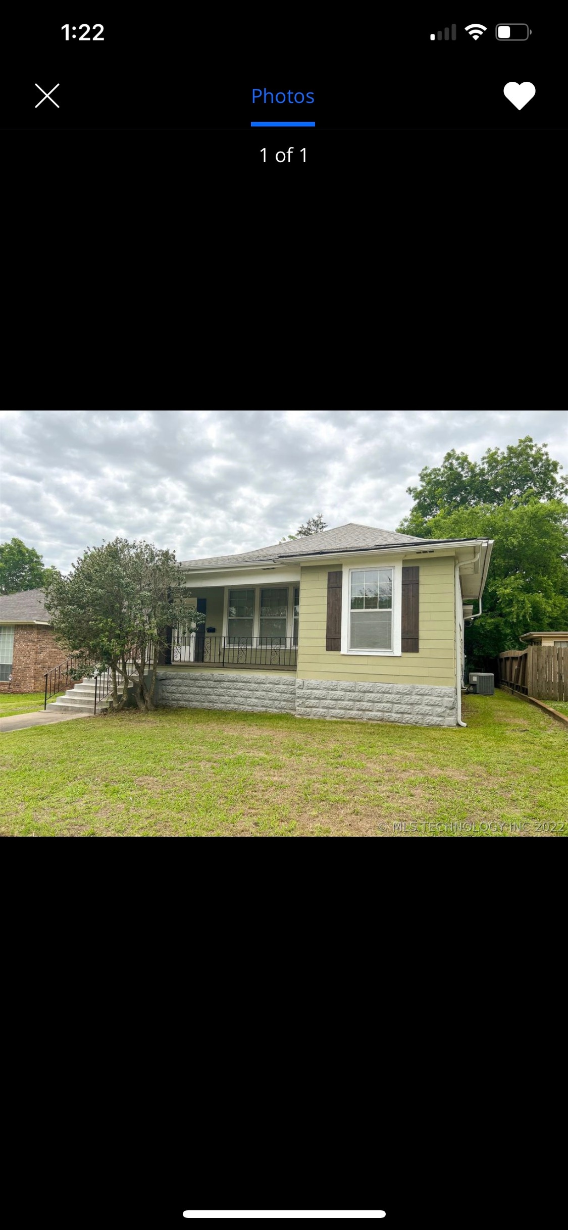 A light yellow house is presented with a simple design and a welcoming front porch. Green grass surrounds the home, and a small bush is visible near the entrance. The cloudy sky reflects a calm atmosphere in the neighborhood.