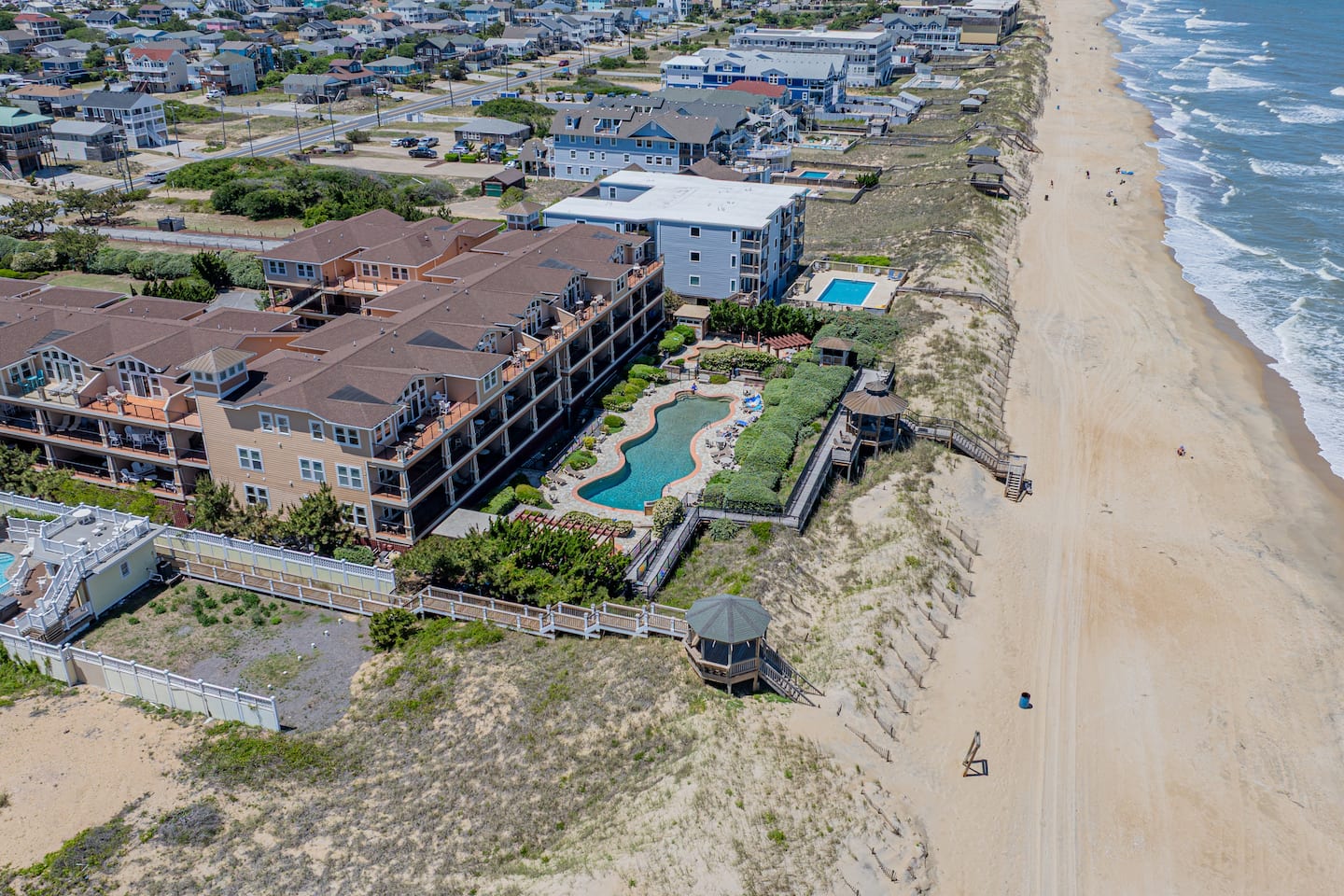 Step back and take in what you're actually booking, the entire Croatan Surf Club resort from above. Freeform pool, splash pad, condo buildings, and the Atlantic right behind it. Your home base for the week is all of this.