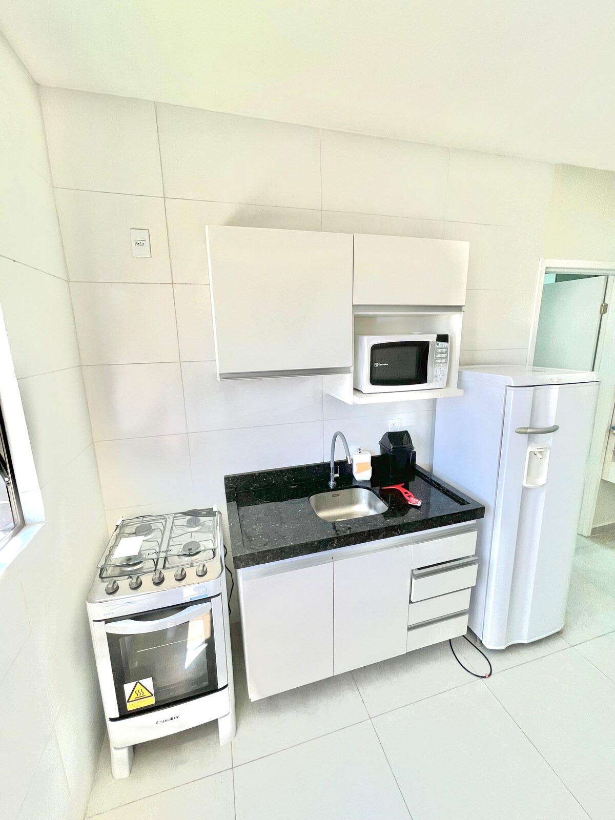 The kitchen area features a sleek design with a black countertop, a four-burner stove, a microwave, and a coffee maker. A refrigerator stands nearby, offering ample storage space. The cabinets above provide additional storage, contributing to a functional cooking environment.