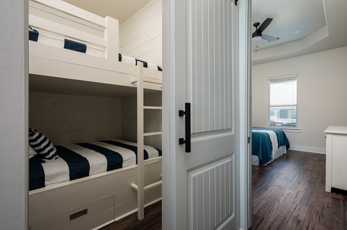 Loft con literas con dos camas completas entre el dormitorio principal y el baño principal. Las literas personalizadas tienen luces y cargadores de teléfono junto a cada cama