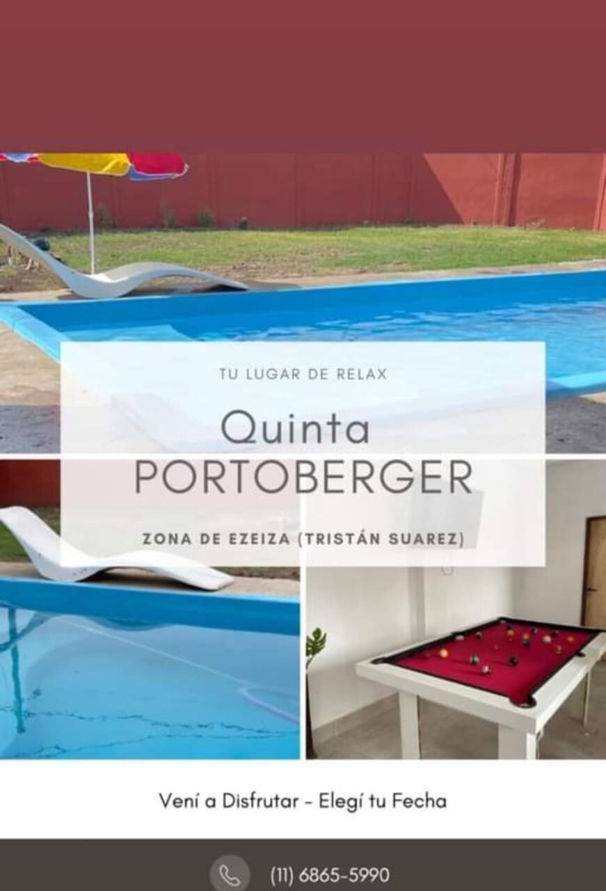 A serene outdoor space features a swimming pool with clear blue water surrounded by a vibrant red fence. A foosball table is visible nearby, providing an option for entertainment. Reflections of the surrounding area can be seen on the smooth pool surface.