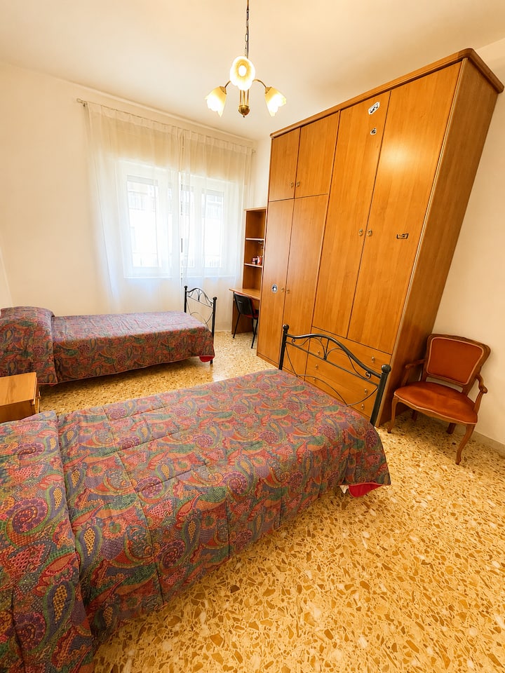 The room has a large wardrobe, a desk, Wi-Fi, and natural light thanks to the large window. A simple, comfortable and functional environment for a pleasant stay.