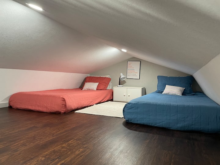 Loft abierto con dos camas individuales, una lámpara y un gabinete con algunos juegos y libros para niños. Hay espacio para jugar en el piso y una barandilla para la seguridad. Esta zona se puede ver desde la cocina y otros loft. 