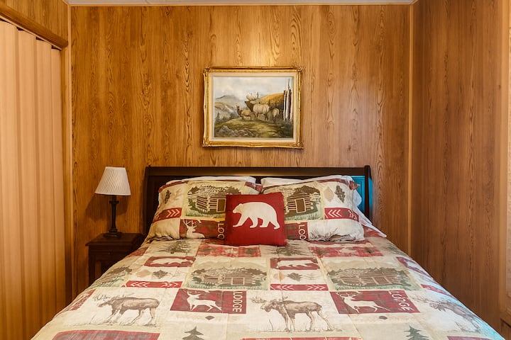 A simple, cozy room with a queen-size bed made with lodge-style bedding and a decorative accent pillow. 