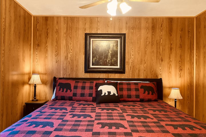 A cozy room with a king-size bed featuring red plaid cabin-themed bedding and matching pillows. 