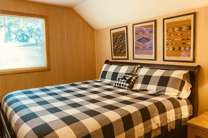 A room with a king-size bed made with plaid bedding and pillows. 
