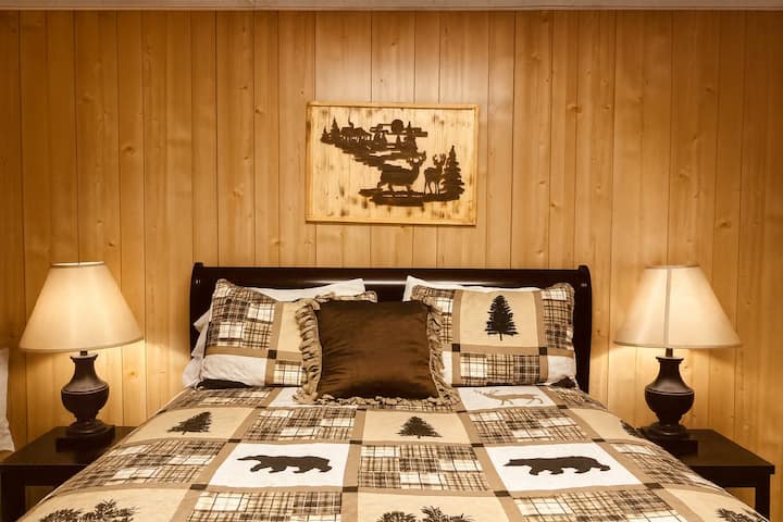 A warm, cabin-style room featuring a king-size bed with patterned bedding and pillows. 