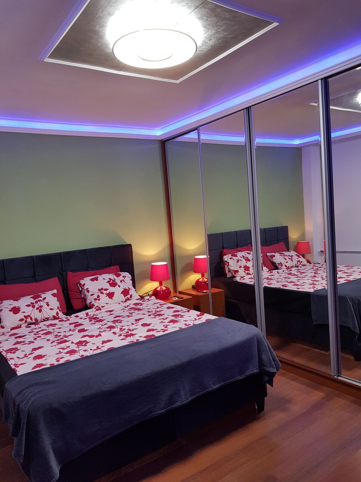 Dhomë gjumi 1 e pajisur me krevat martesor me madhësi mbretërore, televizor inteligjent dhe AC, veshje bujare me pasqyra, tavolinë pune në distancë, drita ambienti, pamje panoramike drejt pjesës së pasme të bllokut. 