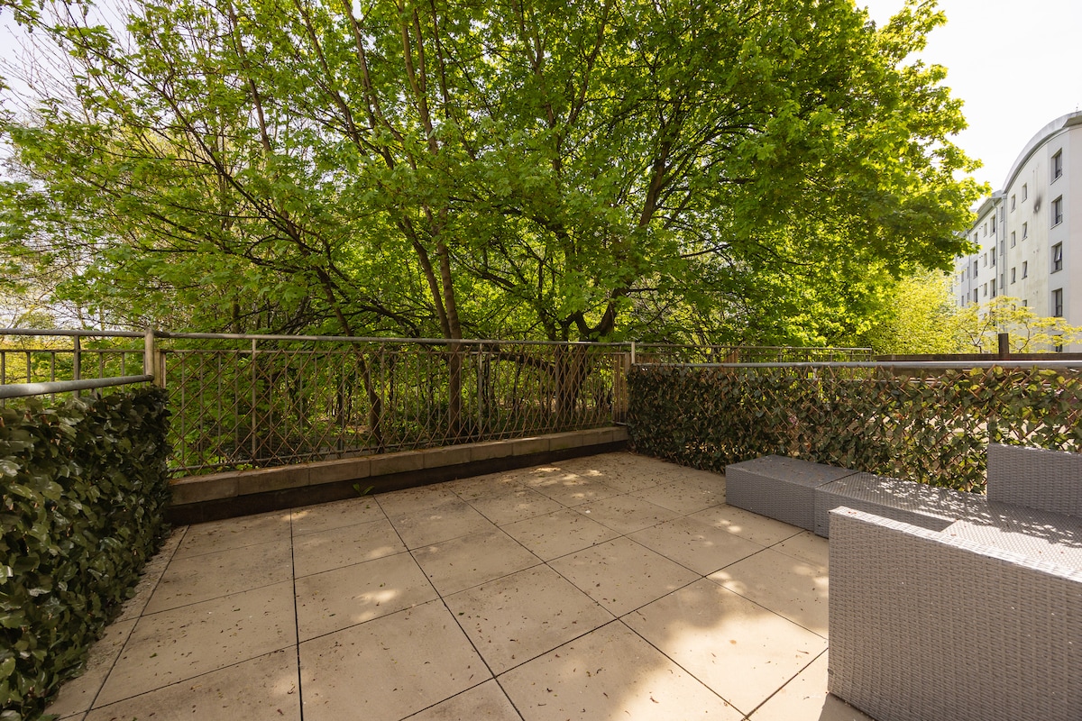 A private patio area features a spacious paved surface surrounded by lush greenery. Outside seating is provided, offering a tranquil space for relaxation. The setting is ideal for enjoying a morning coffee or unwinding after a day of exploring.