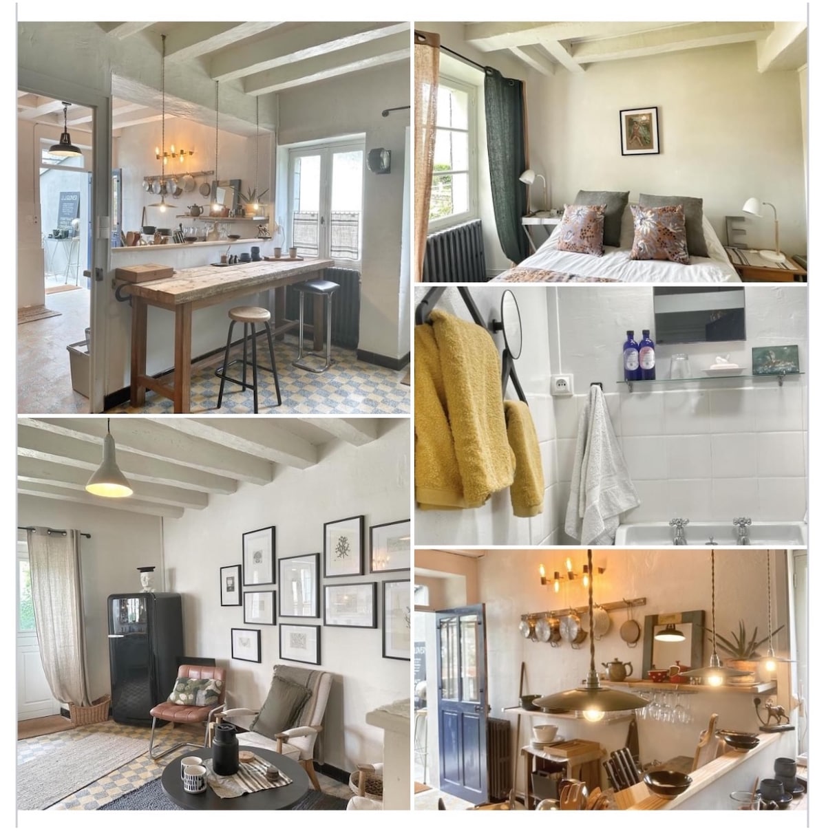 An open plan living area is featured, with a wooden breakfast bar accompanied by high stools. The cozy sleeping area includes a double bed adorned with decorative pillows beside large windows. A modern kitchen corner showcases original art on white walls, accented by soft lighting.