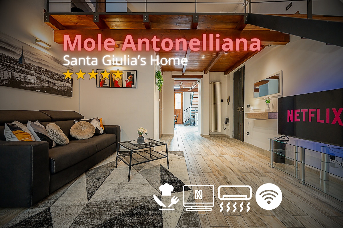 The living area features a dark sofa that can convert into a bed, offering additional sleeping space. A large smart TV with a Netflix logo is visible. Light wooden flooring contrasts with the exposed wooden beams above, contributing to an open and airy environment.