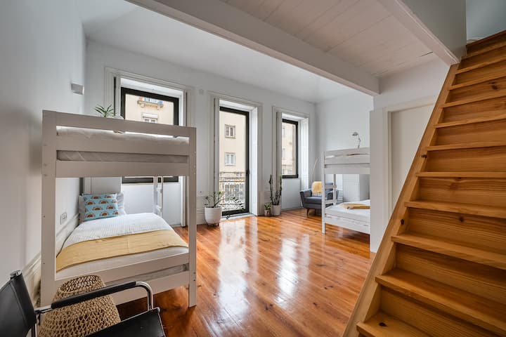 This bright, open space features two bunk beds, a single loft bed, and a private bathroom. The loft is easily accessible via a sturdy staircase, offering a cozy, tucked-away sleeping area.