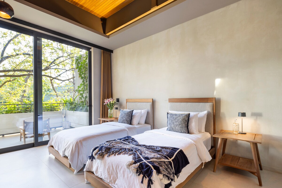 غرفة نوم في أعلى اليمين، مع سرير بحجم كبير أو سريرين منفصلين، ومروحة سقف، وتكييف هواء، وخزانة ملابس مع شماعات وخزنة، ومرآة لكامل الجسم، وسلة غسيل