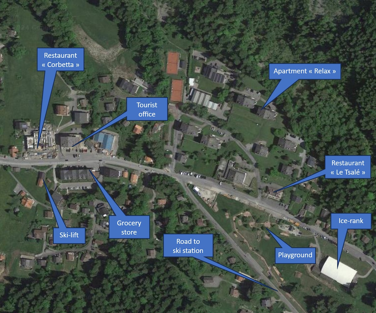 An aerial view of the village, highlighting key locations. Marked points indicate the placement of the apartment, restaurants, a grocery store, a ski-lift, a playground, an ice-rink, and a tourist office, providing an overview of the community amenities.