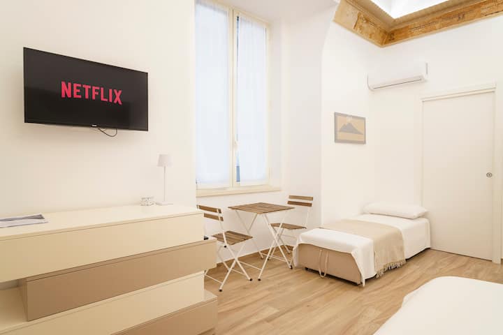 غرفة معيشة مع سرير كرسي بذراعين مفتوح وطاولة قهوة مع كراسي لتناول الطعام مع إطلالة على الشارع النموذجي في نابولي وتكييف هواء ساخن/بارد وتلفزيون ذكي 