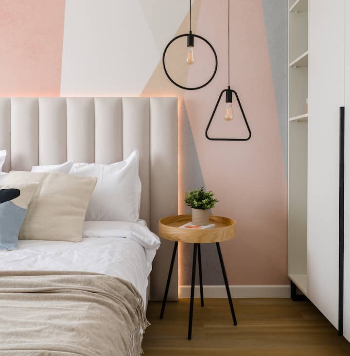 חדר שינה מואר ונשי עם צבעי גוון רך, תאורת תליון לצד המיטה וראש מיטה מודרני. הסידור הנוח יוצר מרחב שינה רגוע ומסוגנן.