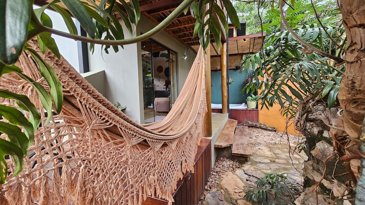 A cozy hammock, crafted from a soft fabric, is suspended on a porch surrounded by lush greenery. The wooden deck features natural stone flooring, providing a tranquil setting for relaxation. The soothing environment invites moments of leisure amidst nature.