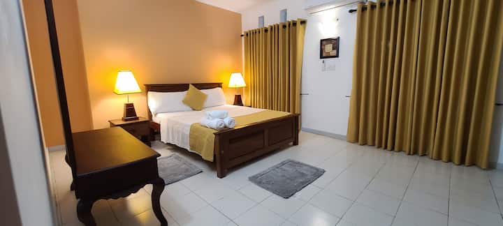 This is the Master Bedroom of the house, it has a ceiling fan, air conditioner, dresser with a mirror, and a wardrobe. 