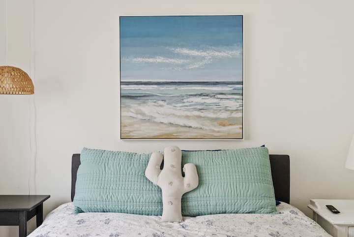 تحتوي غرفة نوم الضيوف في الطابق السفلي على سرير بحجم كوين وفن حائط وتلفزيون ذكي مثبت على الحائط.