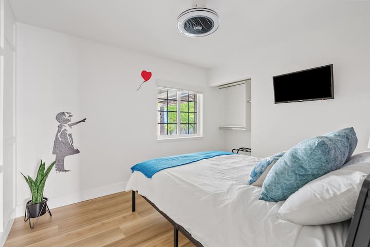 تطل غرفة النوم في الطابق السفلي على الفناء المغطى وتتميز بسرير متوسط الحجم وتلفزيون ذكي مثبت على الحائط. 