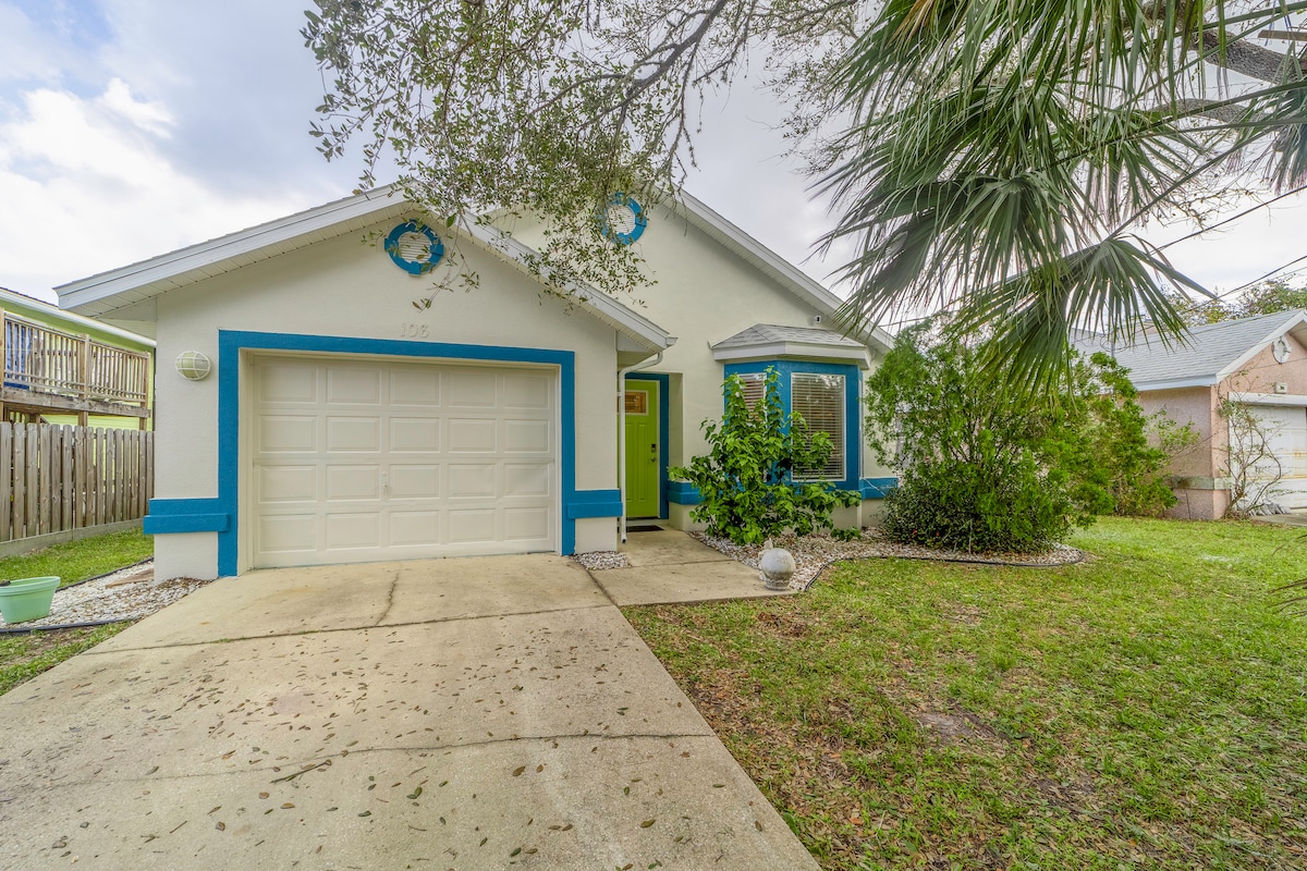The exterior of the vacation home features a vibrant blue trim, large garage, and a welcoming green front door. Lush landscaping with shrubs and palm trees surround the property, enhancing the appeal. A concrete driveway leads to the entrance, with a grassy area in the front yard.