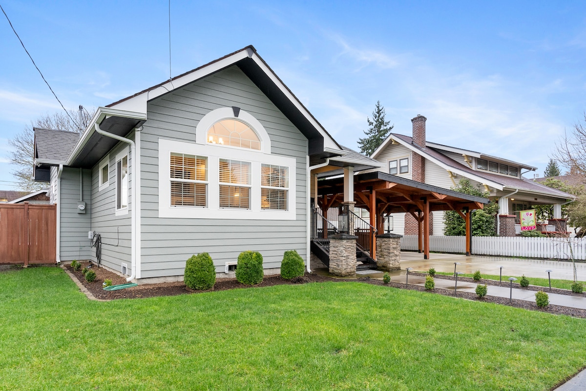 The exterior of the house features a modern grey facade with large front windows, providing ample natural light to the interior. A spacious porch is covered, offering a welcoming entrance. The landscaped yard is adorned with neatly trimmed shrubs, contributing to the overall charm of the property.