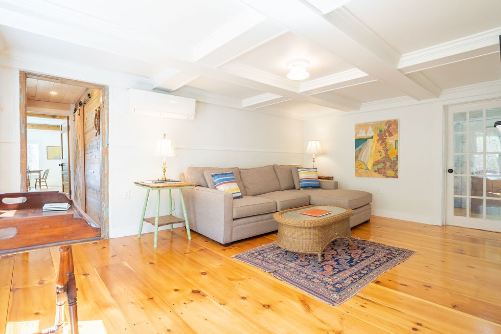 Connected to the addition through an ell, this restored 1880s Cape has a spacious living room with a sectional sofa and a 48-inch smart TV mounted over the mantle opposite the couch. A heat pump provides heating and cooling.