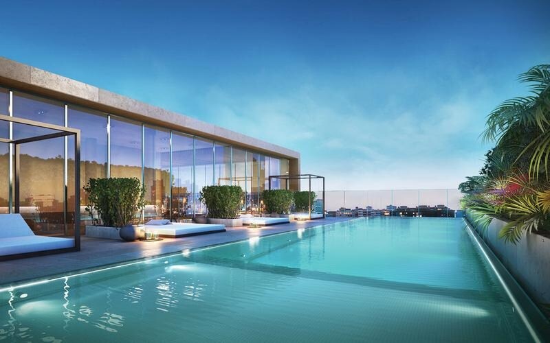 An expansive outdoor pool is featured on the terrace, surrounded by lounge areas and greenery. Glass walls provide a panoramic view of the surroundings, while the serene water reflects the sky, creating a tranquil atmosphere for relaxation.